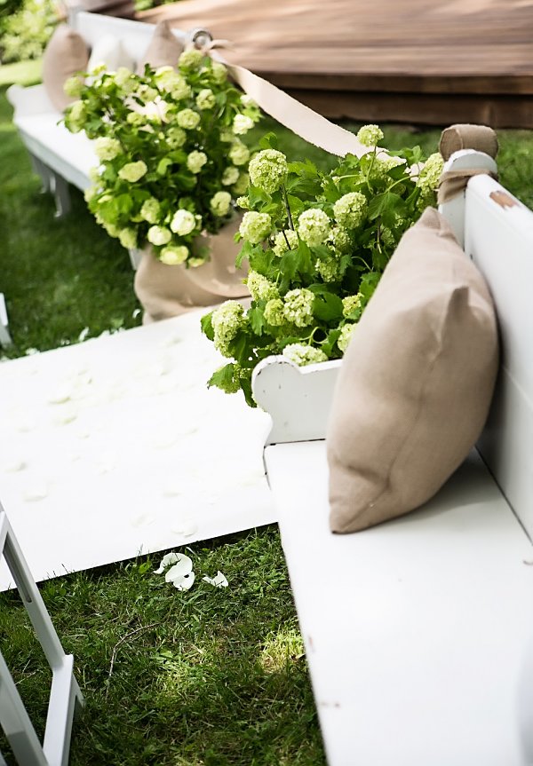 Curated White Pews Event Furniture Rental For Upscale Outdoor Spring Wedding Ceremony With Lush Mounds Of Aisle Flower Arrangements